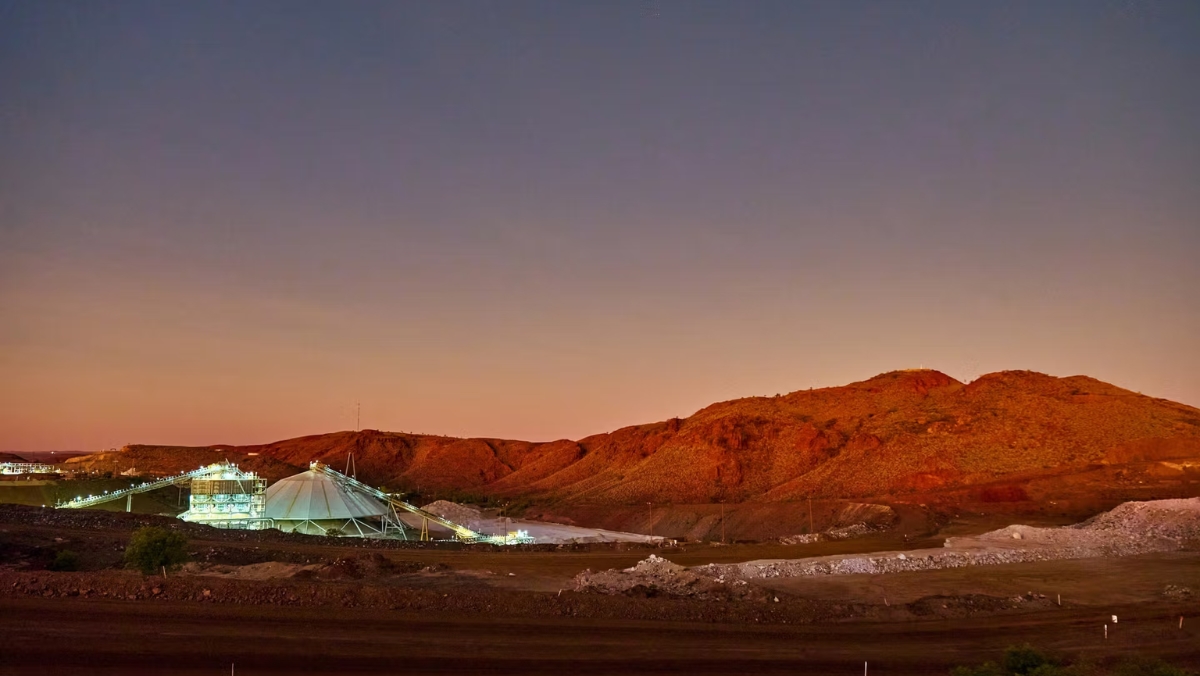 Mining processing plant and conveyor illuminated at dusk against red outback hills
